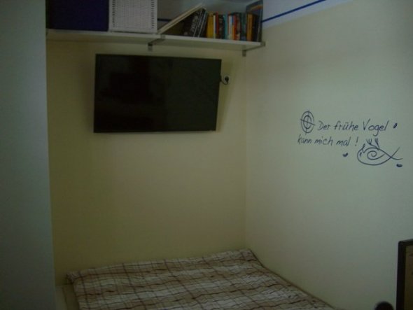 Über dem Fussende vom Bett findet der TV hängend Platz, darüber auf dem Wandbord verschwinden die Bücher.